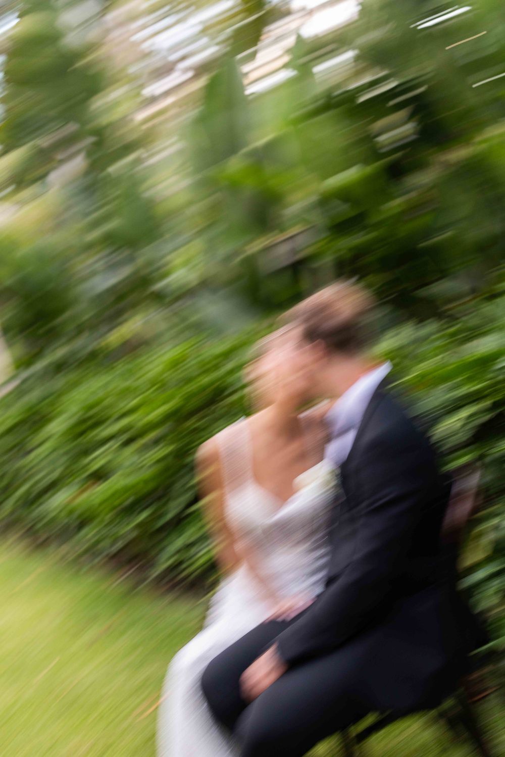 Motion-blurred sequence of bride and groom dancing outdoors with green foliage in background.