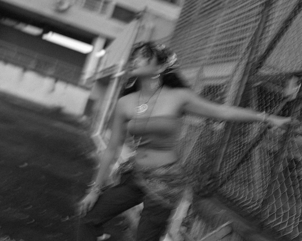Black and white motion blur shot of person dancing or jumping near fence.
