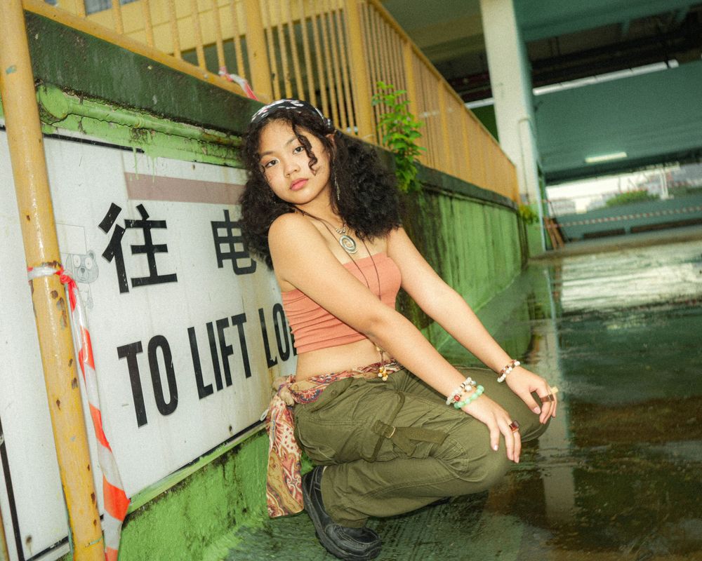 Woman in crop top poses playfully next to 'To Lift' sign in urban setting.