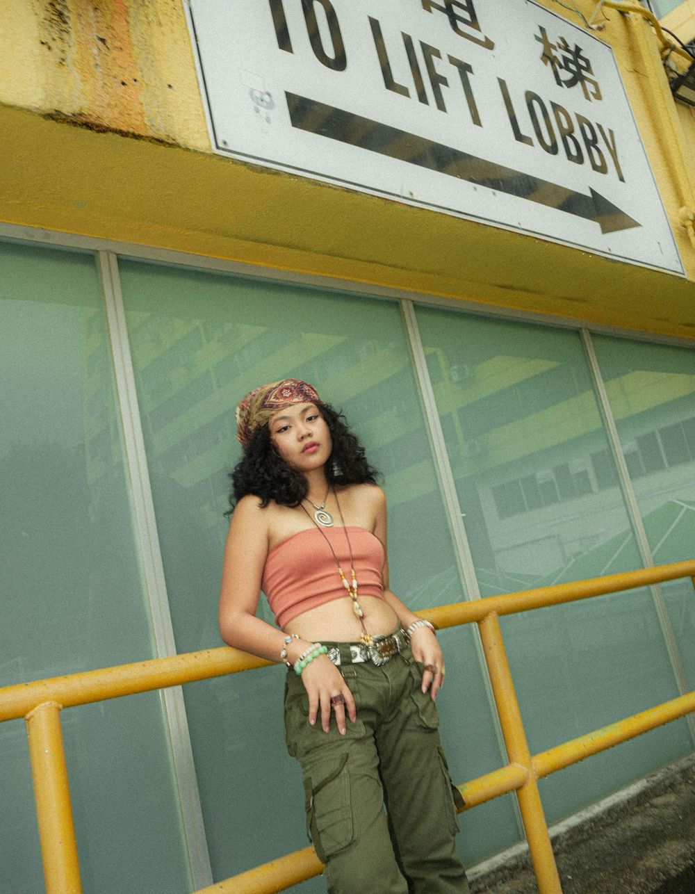 Urban fashion photoshoot at a lift lobby entrance with yellow railings and signage.