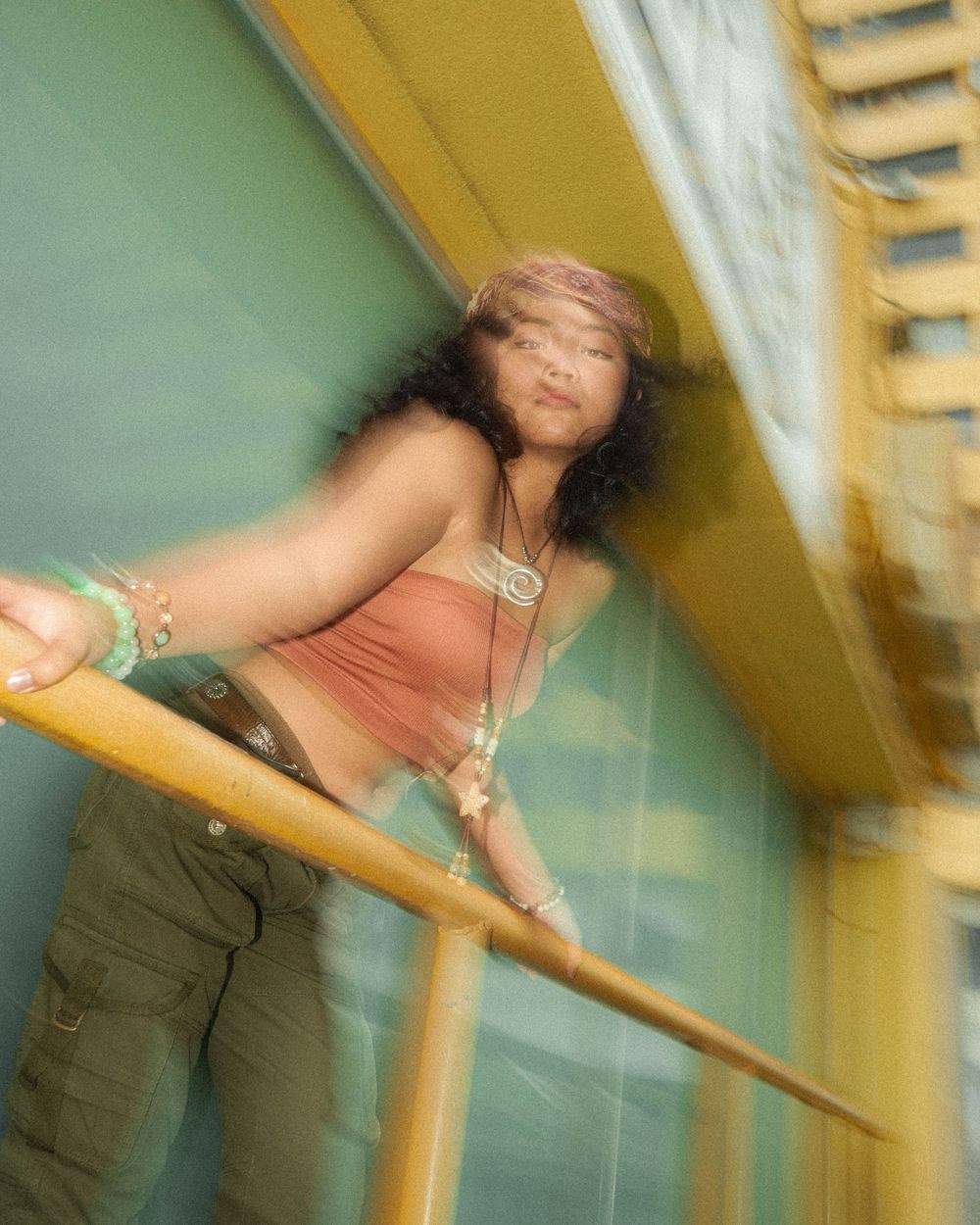 Dynamic fashion portrait with motion blur against a yellow and green architectural background.