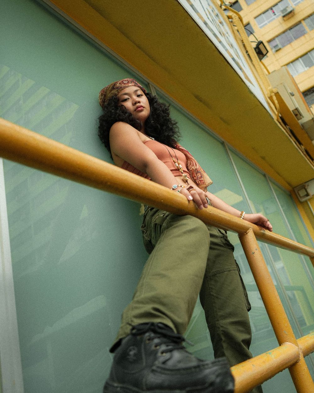 Low angle fashion portrait against yellow railings and urban architecture.