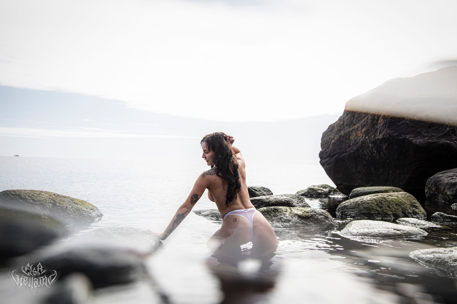 A dreamy bridal portrait captured among coastal rocks with misty ocean atmosphere in soft ethereal lighting.