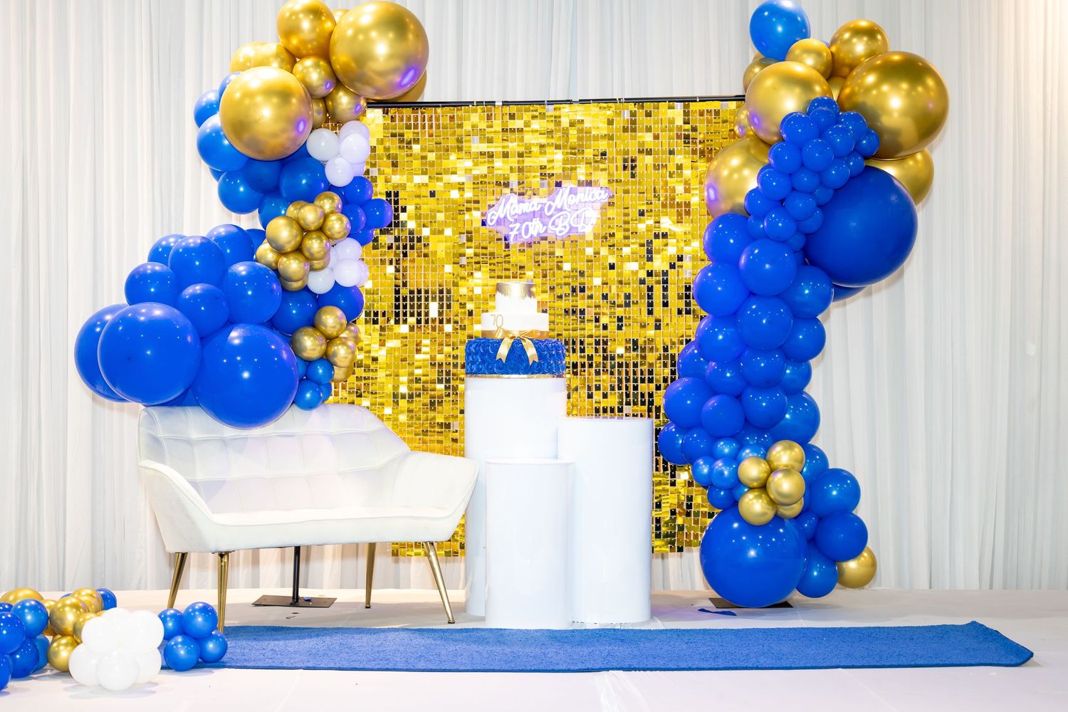Elegant party decor featuring a blue and gold balloon arch with white pedestals.