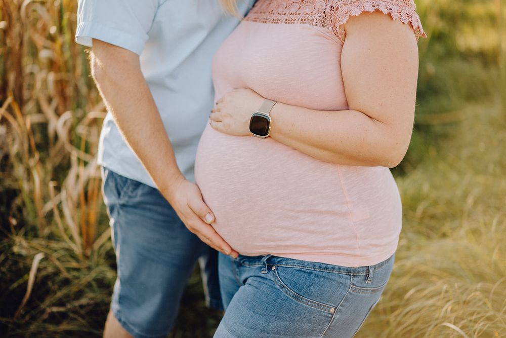 Close-up shot of expecting parents' hands resting on a baby bump against golden sunlight.