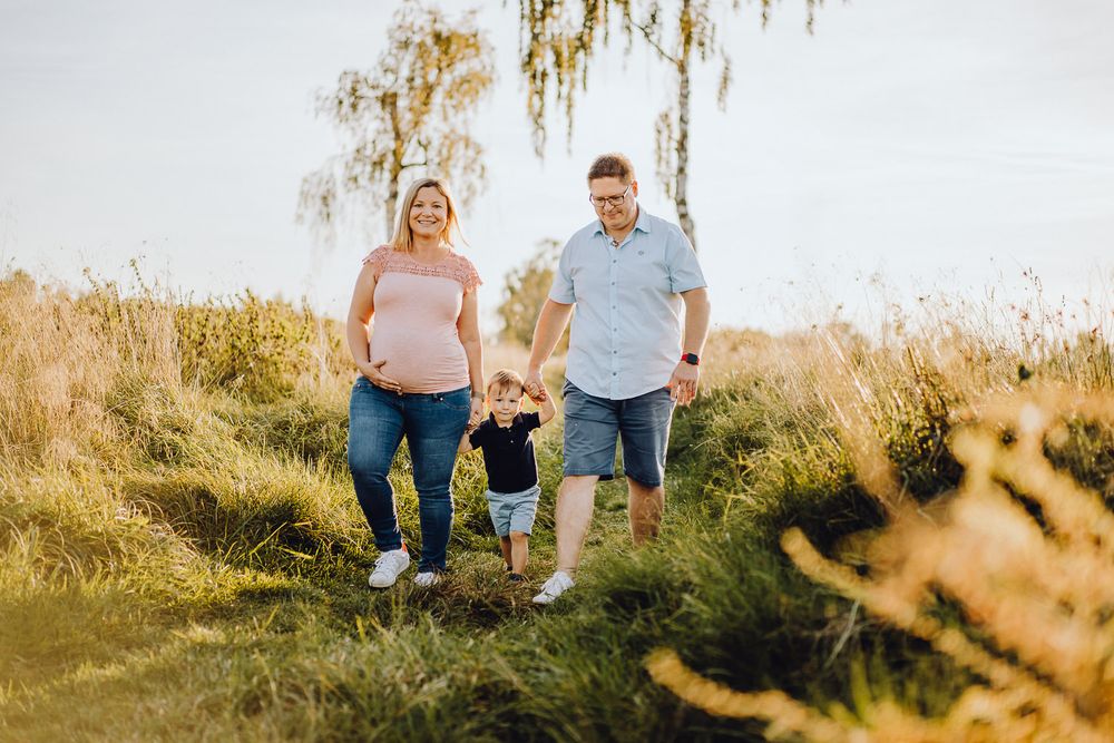 Family walking together through tall grass on a sunny hillside path.