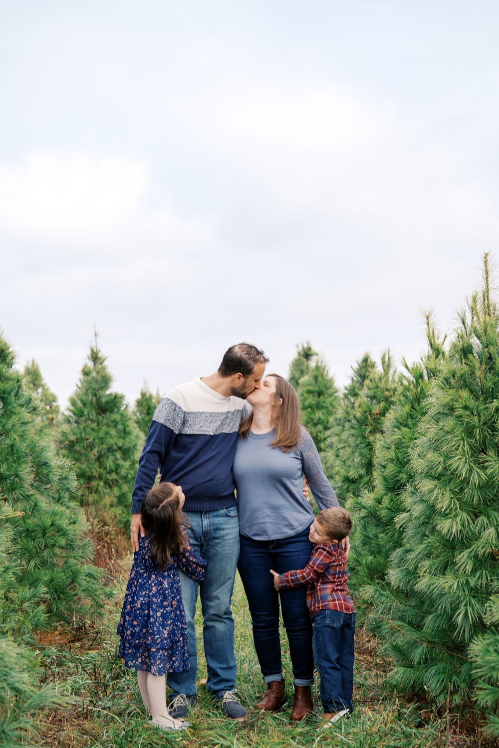 A family shares an intimate moment while standing between rows of Christmas trees.