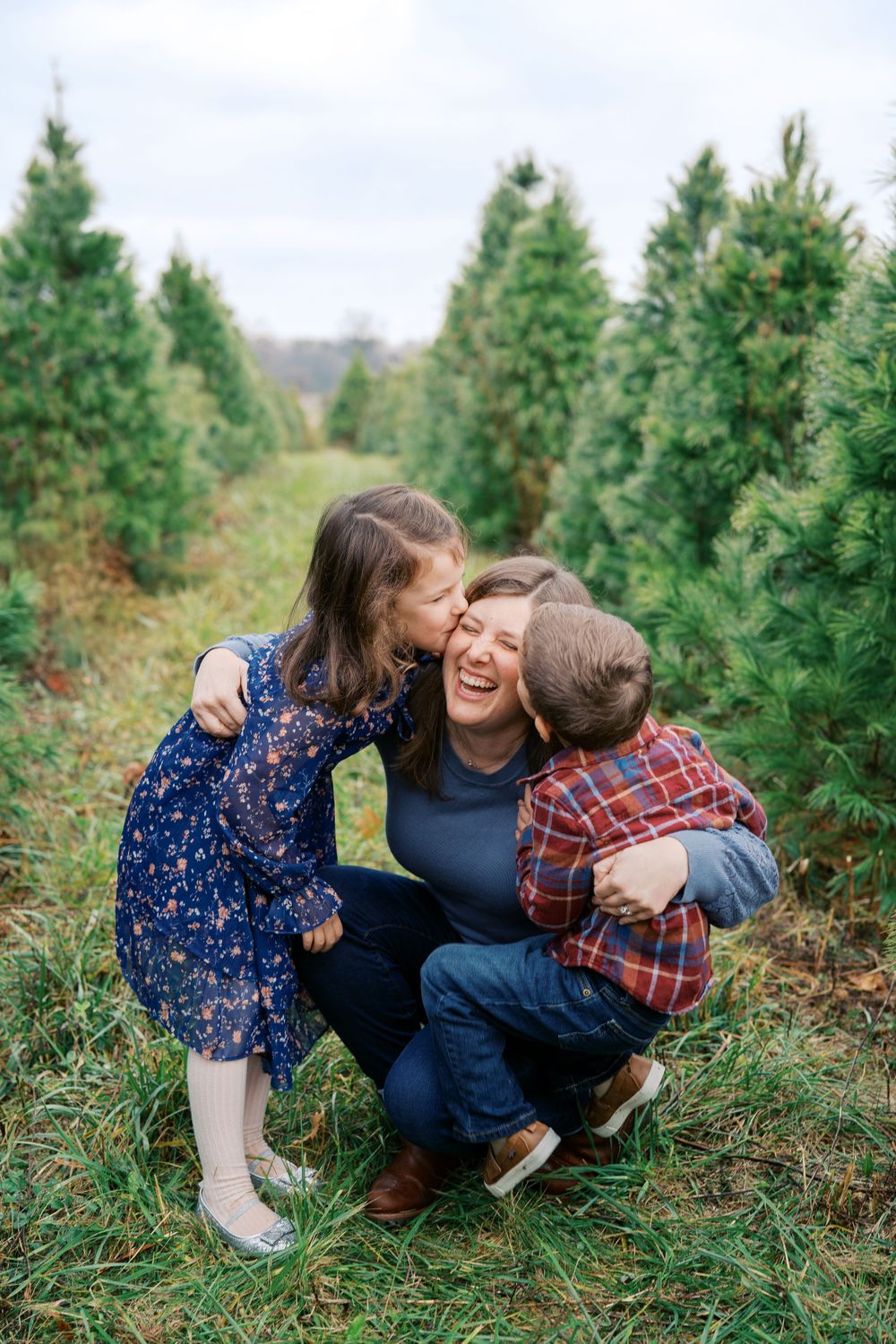 A joyful family moment captured between rows of evergreen trees at a Christmas tree farm.