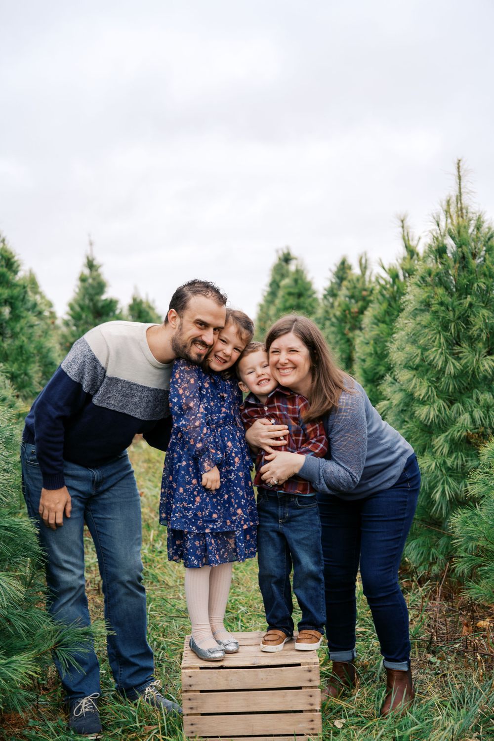 Family shares loving moments together on wooden crates at a Christmas tree farm.