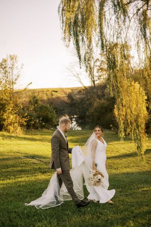 A couple walks beneath golden willow trees during their autumn wedding photoshoot.