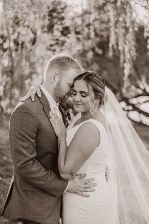 An intimate black and white portrait captures a tender wedding moment outdoors.