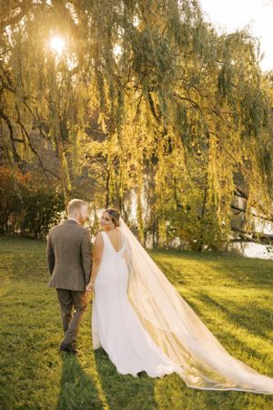 A romantic sunset photo of newlyweds beneath flowing willow branches.