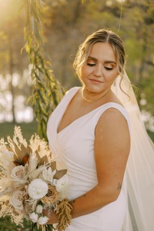 A bride holds a neutral-toned bouquet featuring pampas grass and roses in autumn light.