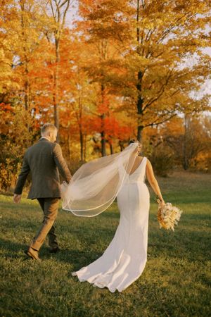 A flowing veil trails behind newlyweds walking through autumn foliage.