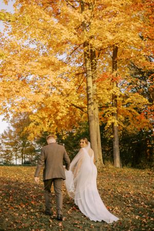 A couple walks hand in hand beneath vibrant golden autumn trees.