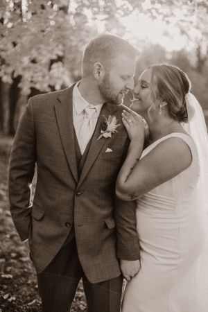 Black and white wedding portrait showing intimate moment between newlyweds in outdoor autumn setting.