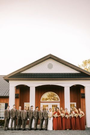 Wedding party in gray suits and burgundy dresses posed in front of white building with columns.