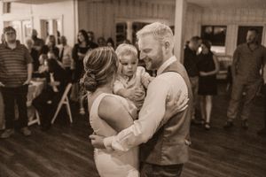 Sepia-toned image of couple dancing at wedding reception while holding small child.
