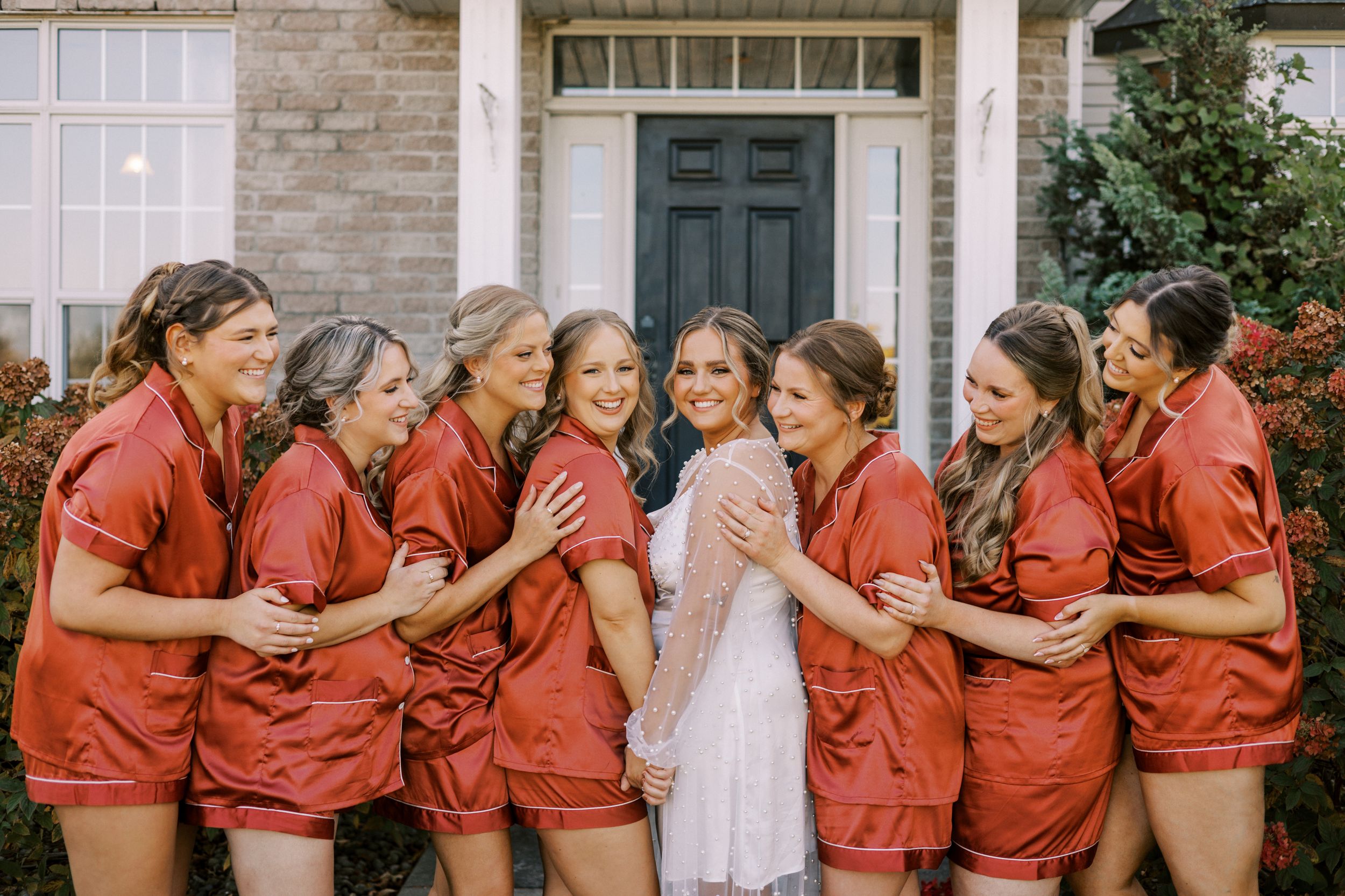 Wedding party in matching red robes shares a joyful moment with the bride.