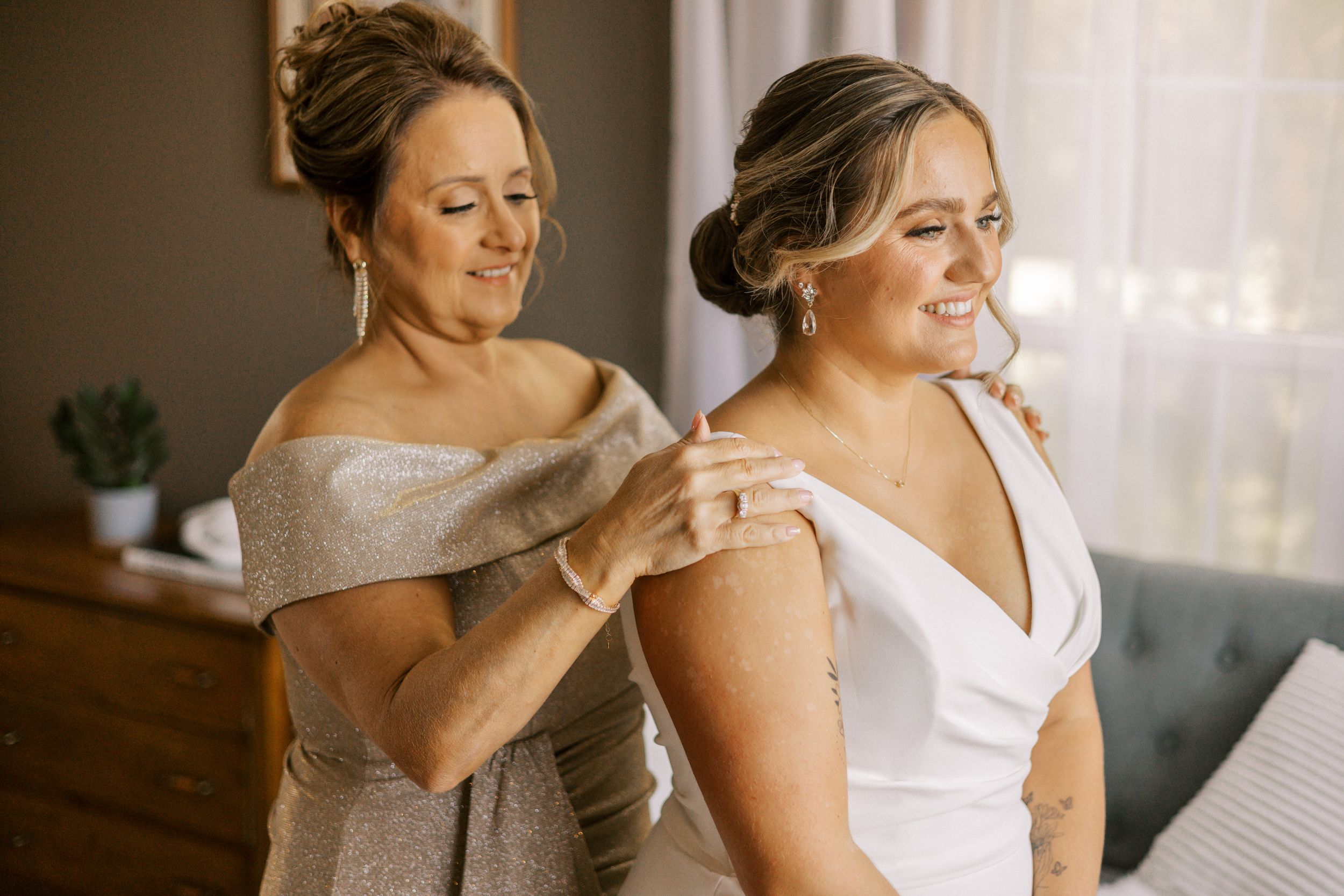 Two women share an emotional getting-ready moment in elegant wedding attire.
