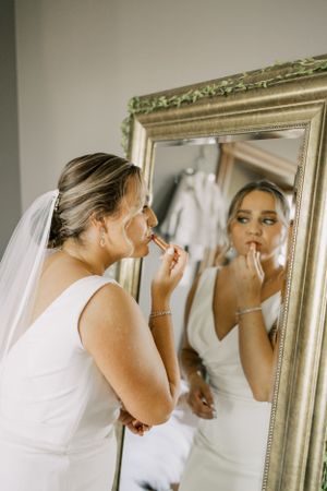 A wedding morning reflection shows final makeup touches being applied in an ornate gold mirror.