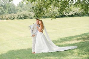 Bride and groom embrace on lush green lawn, her white gown and veil flowing in soft natural light. Married at the Jefferson in Oxford, MS.