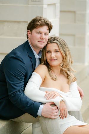 A couple posing closely together against a stone wall in elegant attire. Engagement session on the Square in Oxford, Mississippi.