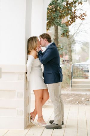 A couple sharing a romantic kiss against a white column on a porch. Engagement session in Oxford, Mississippi.