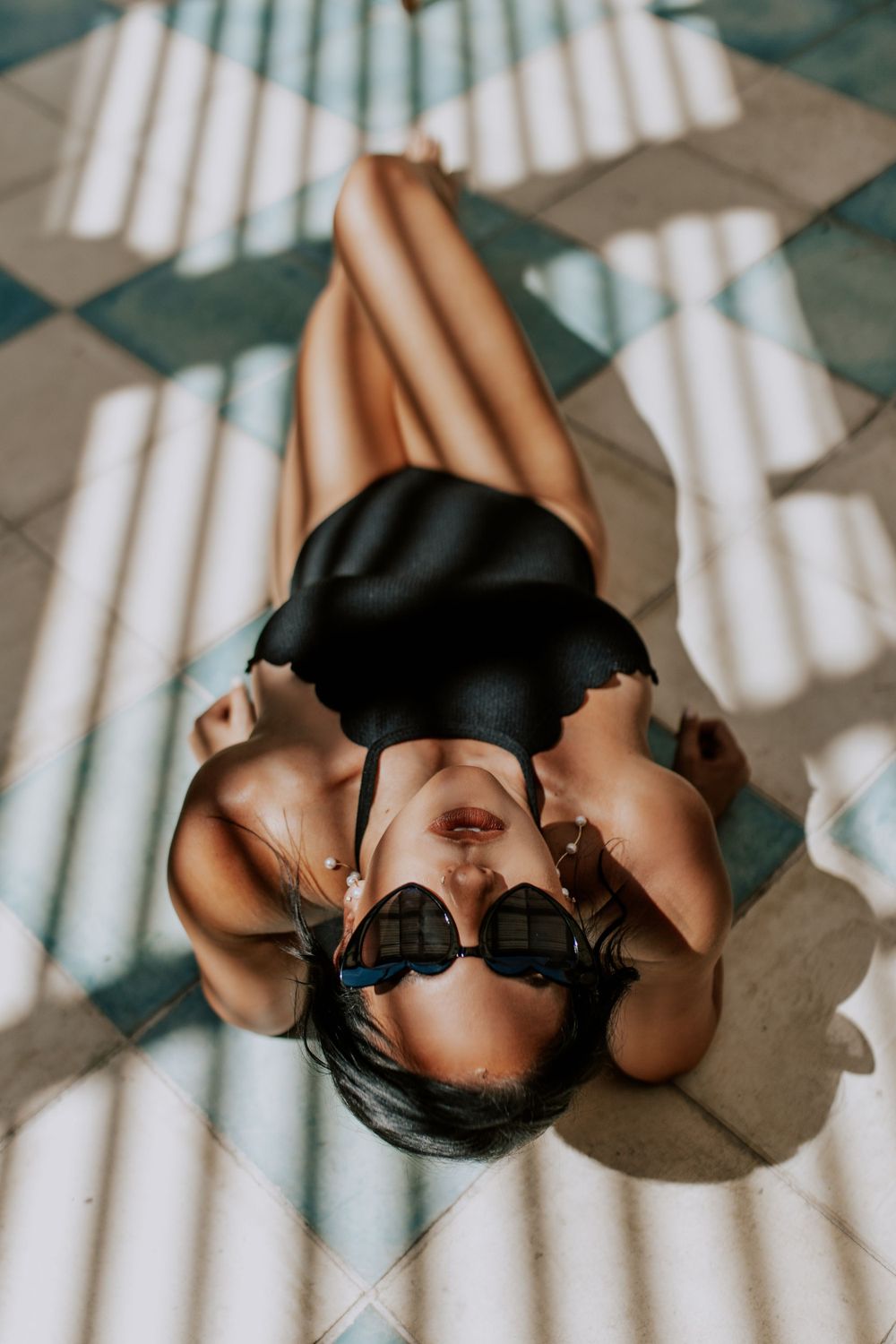 Artistic portrait with dramatic window light casting geometric shadows and highlights on a relaxed figure lying on a floor pattern.