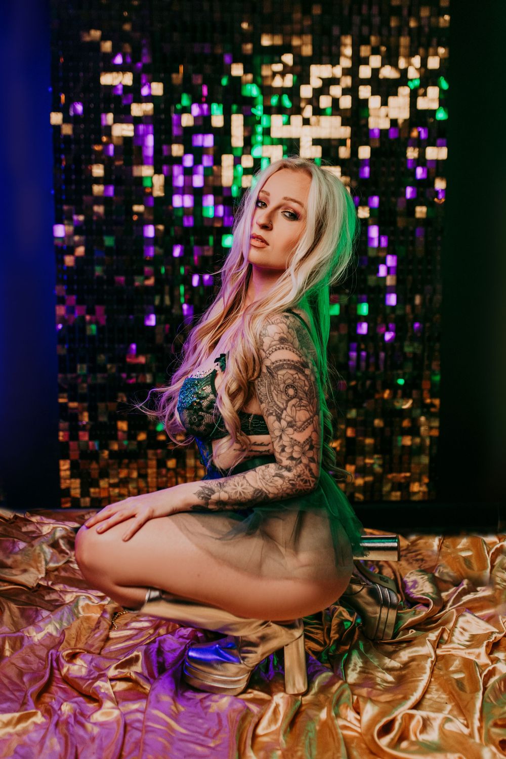 A boudoir photoshoot featuring colorful bokeh lighting effects and metallic gold fabric as backdrop and styling elements.