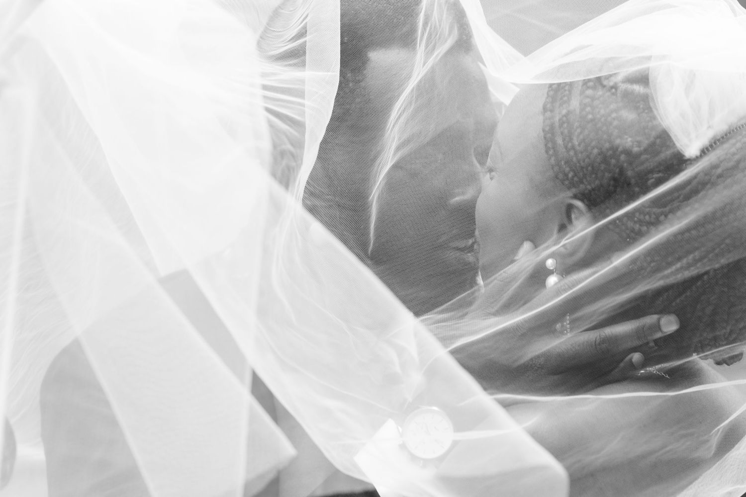 Romantic black and white photo of newlyweds kissing beneath a flowing bridal veil.