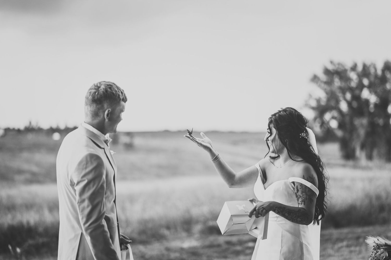 Black and white photo of bride and groom sharing a butterfly release during a wedding ceremony.