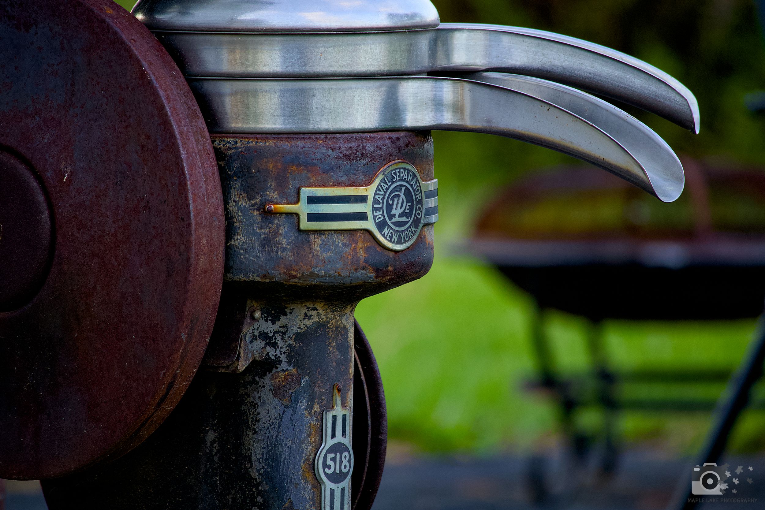 Close-up of a rusty vintage cream separator against green background.