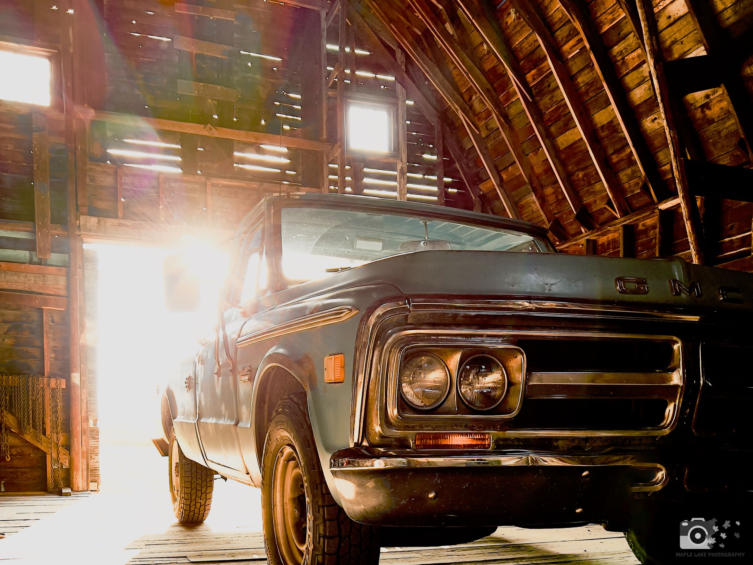 Vintage GMC pickup truck bathed in dramatic sunlight inside a wooden barn.