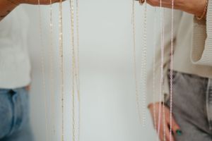 Delicate gold necklaces hanging against a white background in subtle lighting.