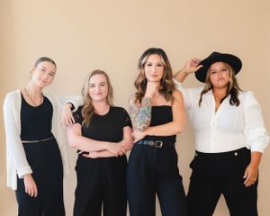 Professional team of four women in coordinated black and white outfits against neutral background.