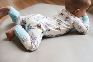 Baby wearing patterned onesie with blue socks lies on grey surface.
