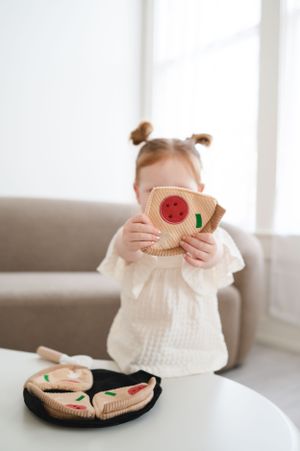 A young child playing with knitted toys on a white table while wearing a cream sweater and buns hairstyle.