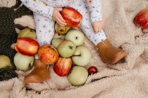 Hand reaching for fresh apples and fruit scattered on beige blanket.