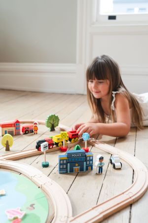 Child playing with detailed wooden train set featuring miniature buildings and trees.
