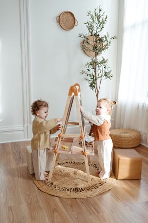 Children playing at wooden easel on round jute rug with wall-mounted baskets and greenery.