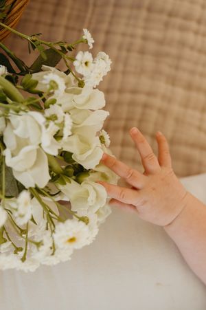 Small hand reaching towards elegant white floral arrangement against textured background.