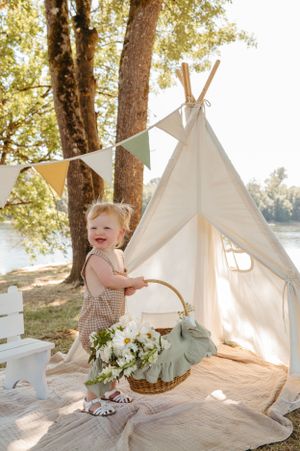 White teepee tent with bunting and floral basket setup outdoors by water.