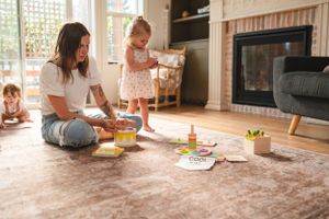 Parent and child playing with educational toys on carpeted floor near fireplace.