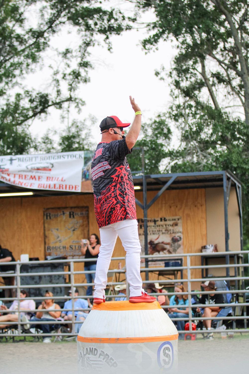 Performer stands triumphantly on orange barrel during rodeo entertainment show.