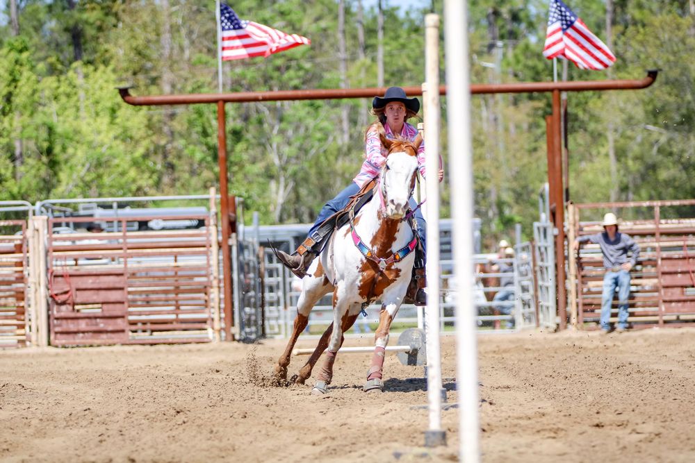 Horseback rider competing in a rodeo arena with American flags flying.
