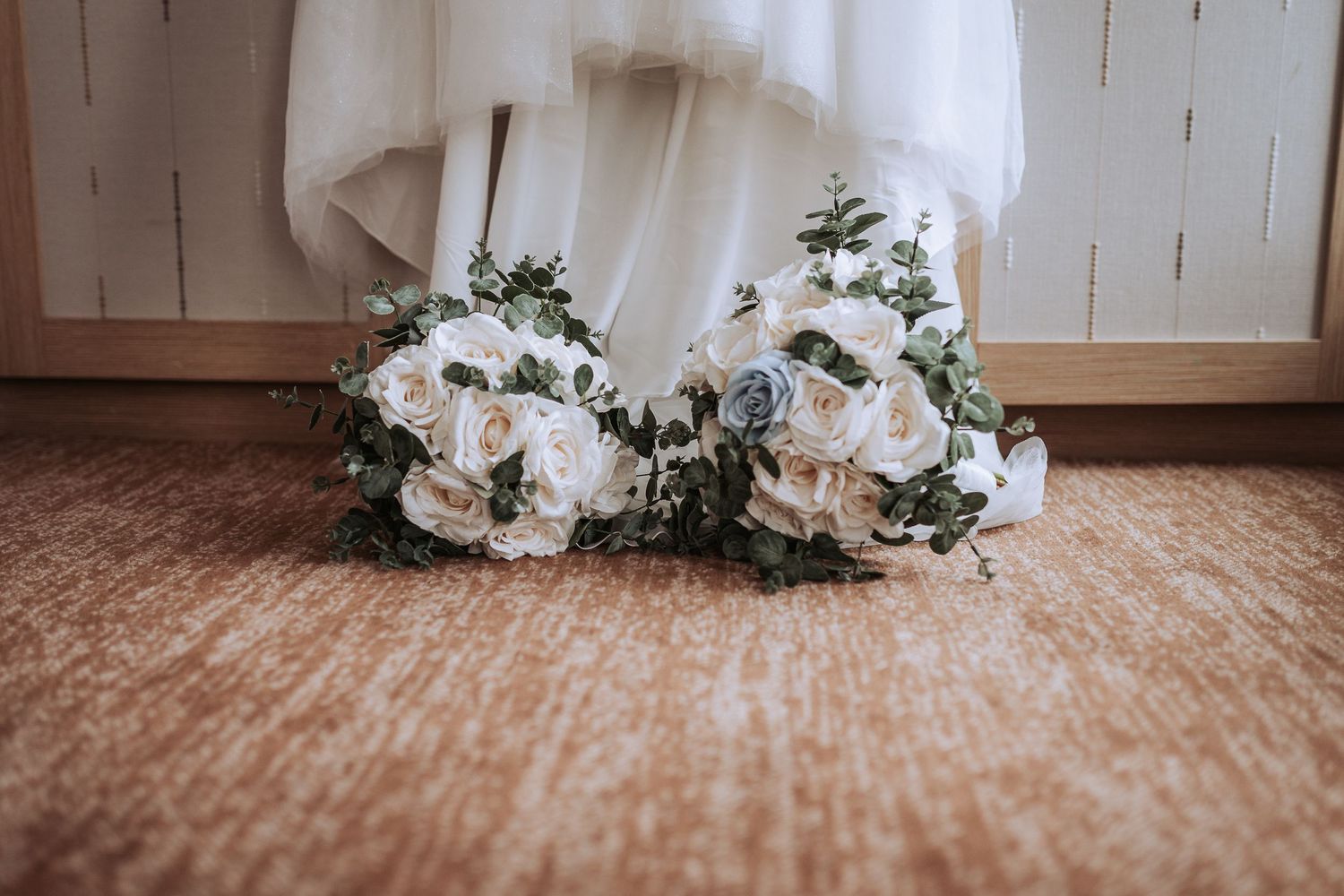 Wedding dress hem and floral bouquets arranged on a rustic wooden floor.