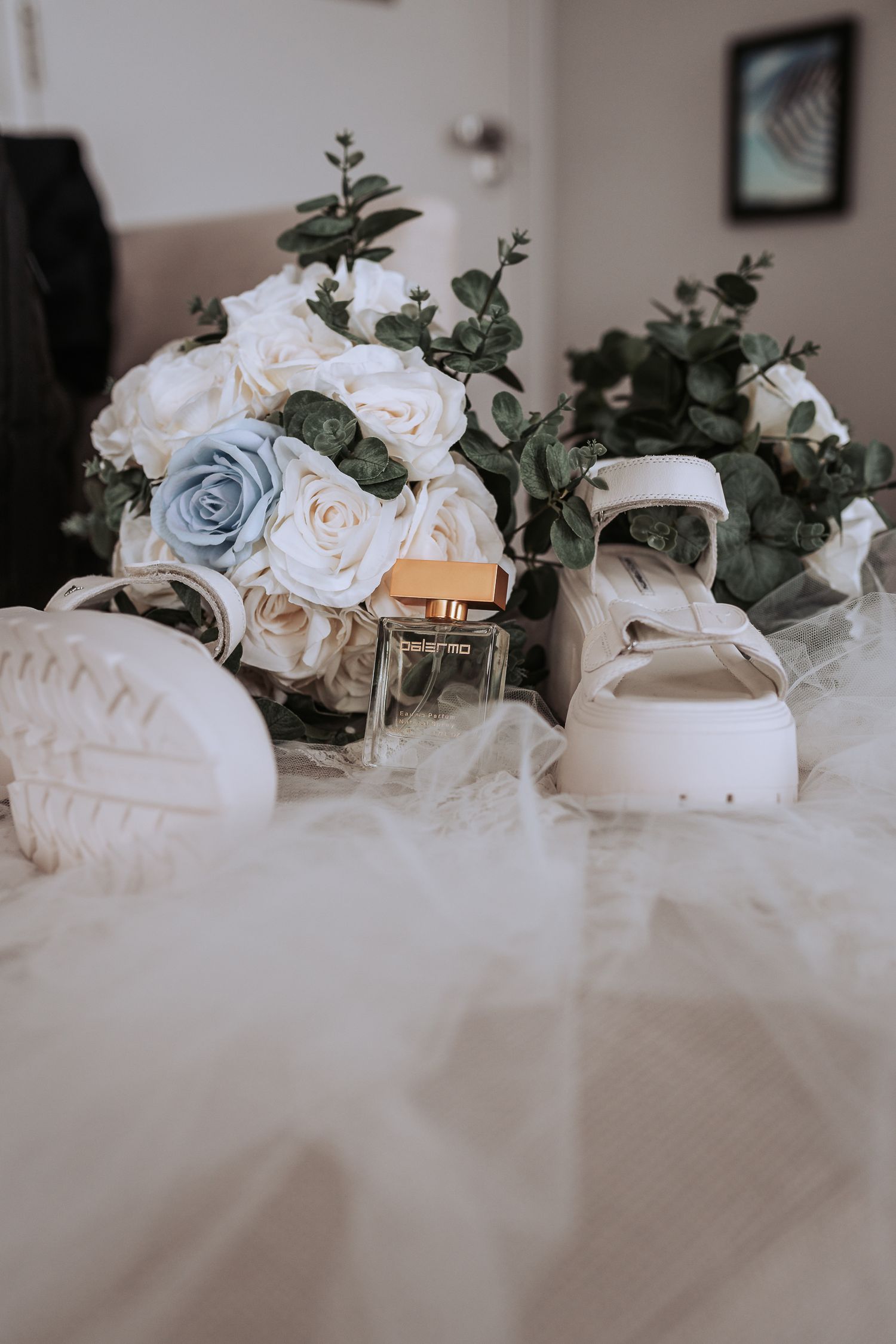 Wedding decor featuring pale roses and eucalyptus with candles on a white surface.