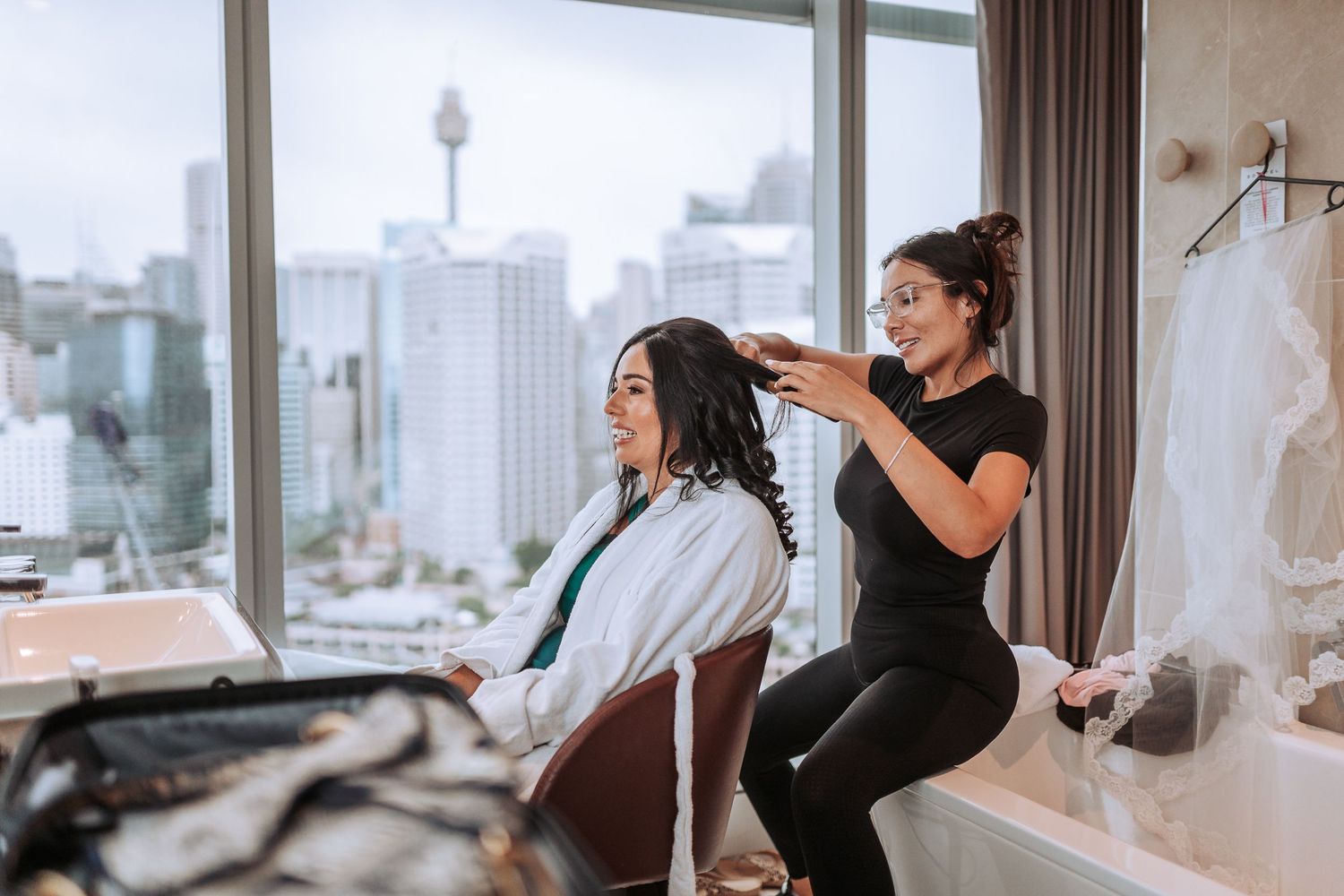 Bridal preparation in a high-rise room with city views through large windows.