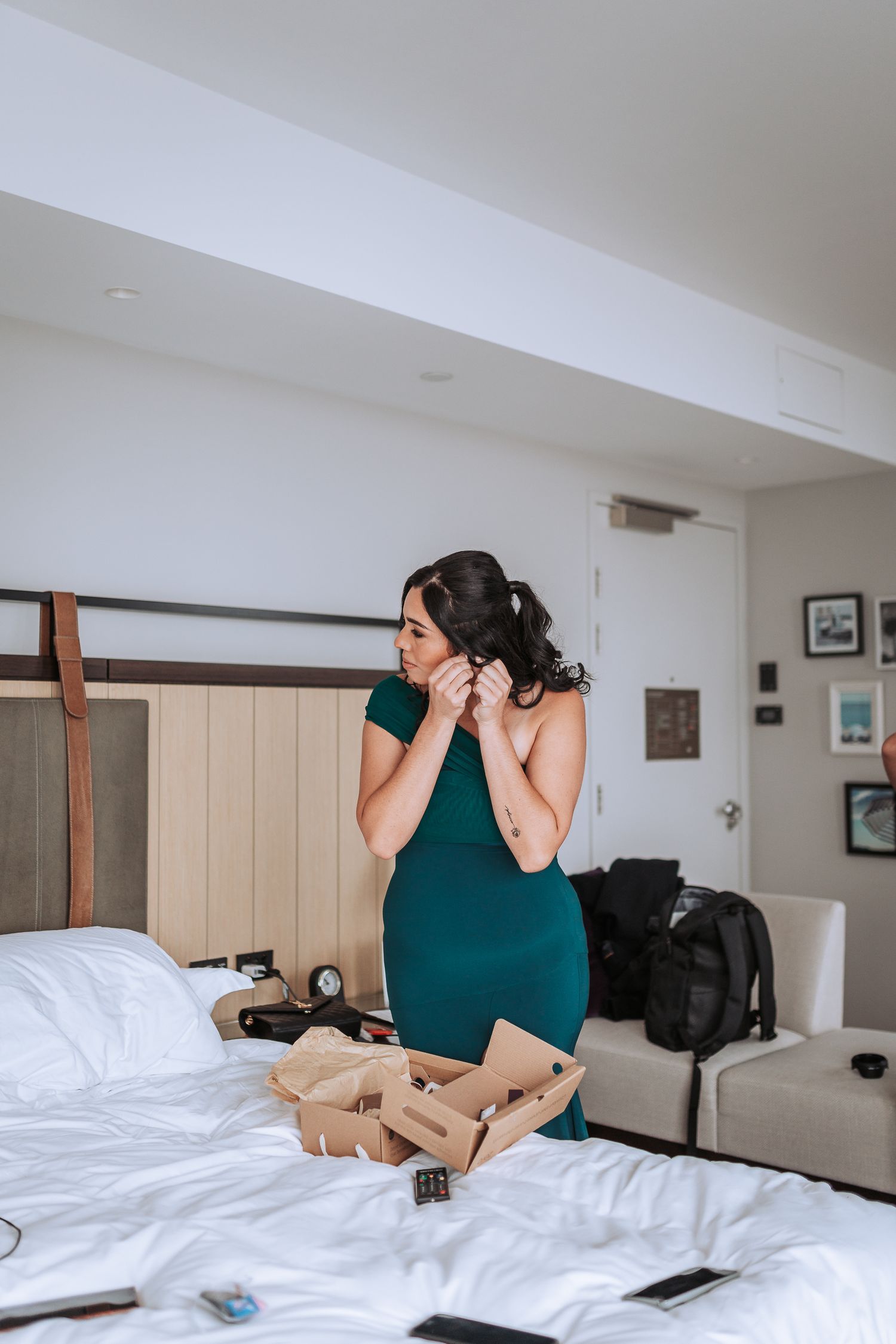 A person in an emerald green dress stands on a hotel bed surrounded by scattered items.